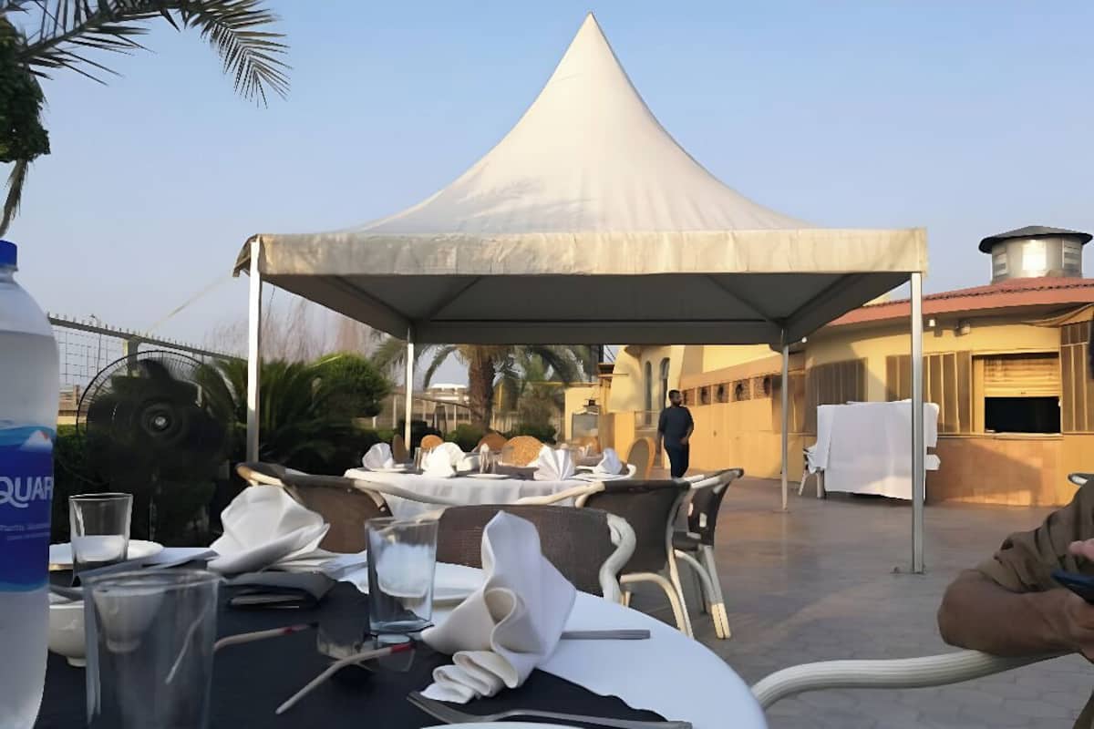 A tented outdoor dining area with tables set for a meal, a water bottle, and a person in the background.