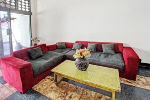 A red sectional sofa with grey cushions, a yellow coffee table, and a vase with flowers. - Hotel O Motel Langko (Mataram)