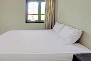 Ein Zimmer mit einem Einzelbett, einem Fenster, Vorhängen und einer schlichten Wand.