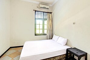 Una cama individual con ropa de cama blanca, una mesita de noche pequeña, una ventana con cortinas y un equipo de aire acondicionado en la pared.