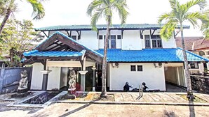 A two-story building with a blue tiled roof, a covered porch, and a statue in front. - Hotel O Motel Langko (Mataram)