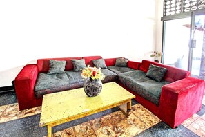 A red sectional sofa with grey cushions, a yellow coffee table, and a vase with flowers. - Hotel O Motel Langko (Mataram)