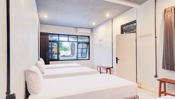 Habitación de hotel con dos camas, una ventana con cortinas, un aire acondicionado instalado en la pared y una puerta con cortina.