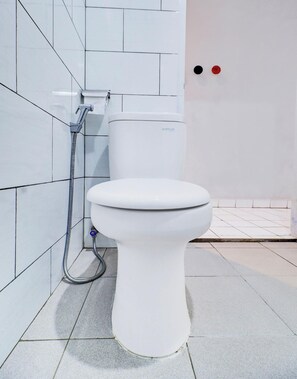 Inodoro blanco con palanca de descarga y manguera, sobre un pared de azulejos.