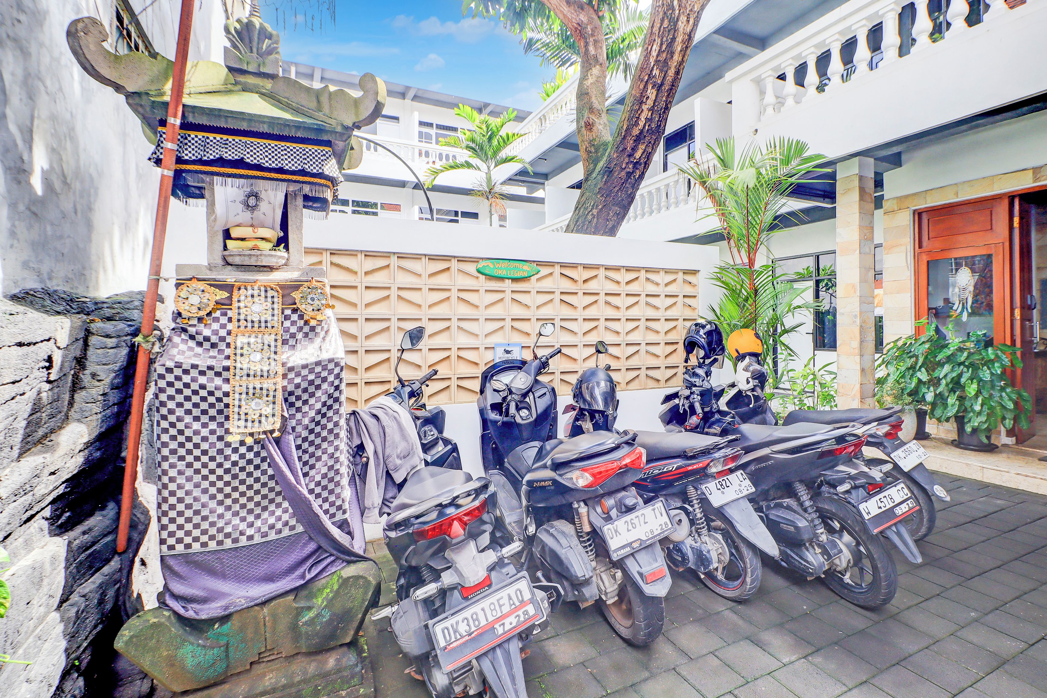 A row of parked motorcycles with visible license plates, a checkered cloth, and a decorative wall with a welcome sign.