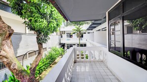 Un balcón techado al aire libre con piso de baldosas, barandillas blancas y vista a un edificio con varias ventanas y balcones.