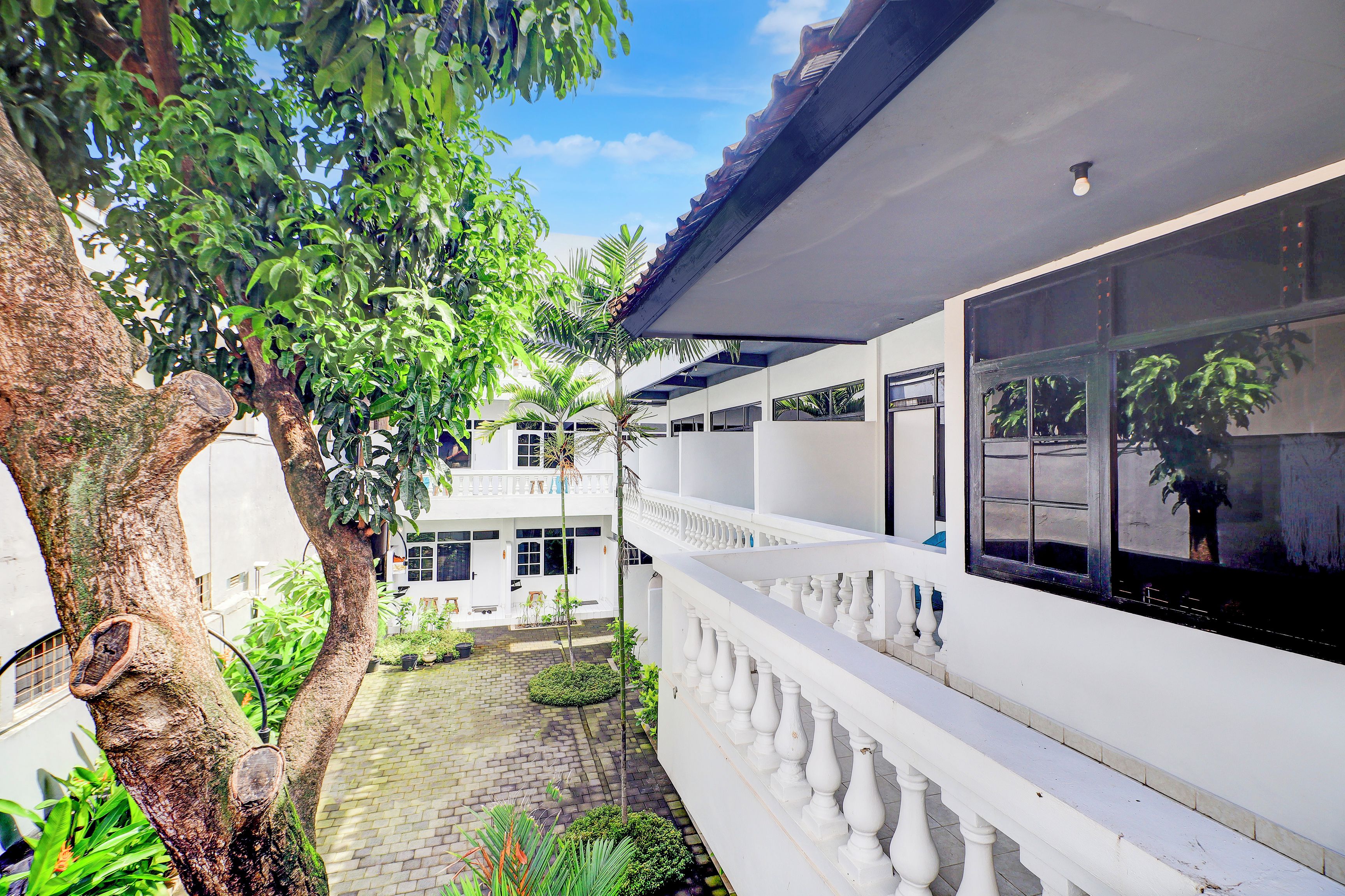Un patio con un edificio blanco, un árbol y una barandilla blanca.