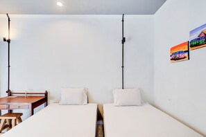 Una habitación pequeña y limpia con dos camas individuales, un escritorio de madera y una silla. Hay dos lámparas fijadas a la pared y un cuadro pequeño.