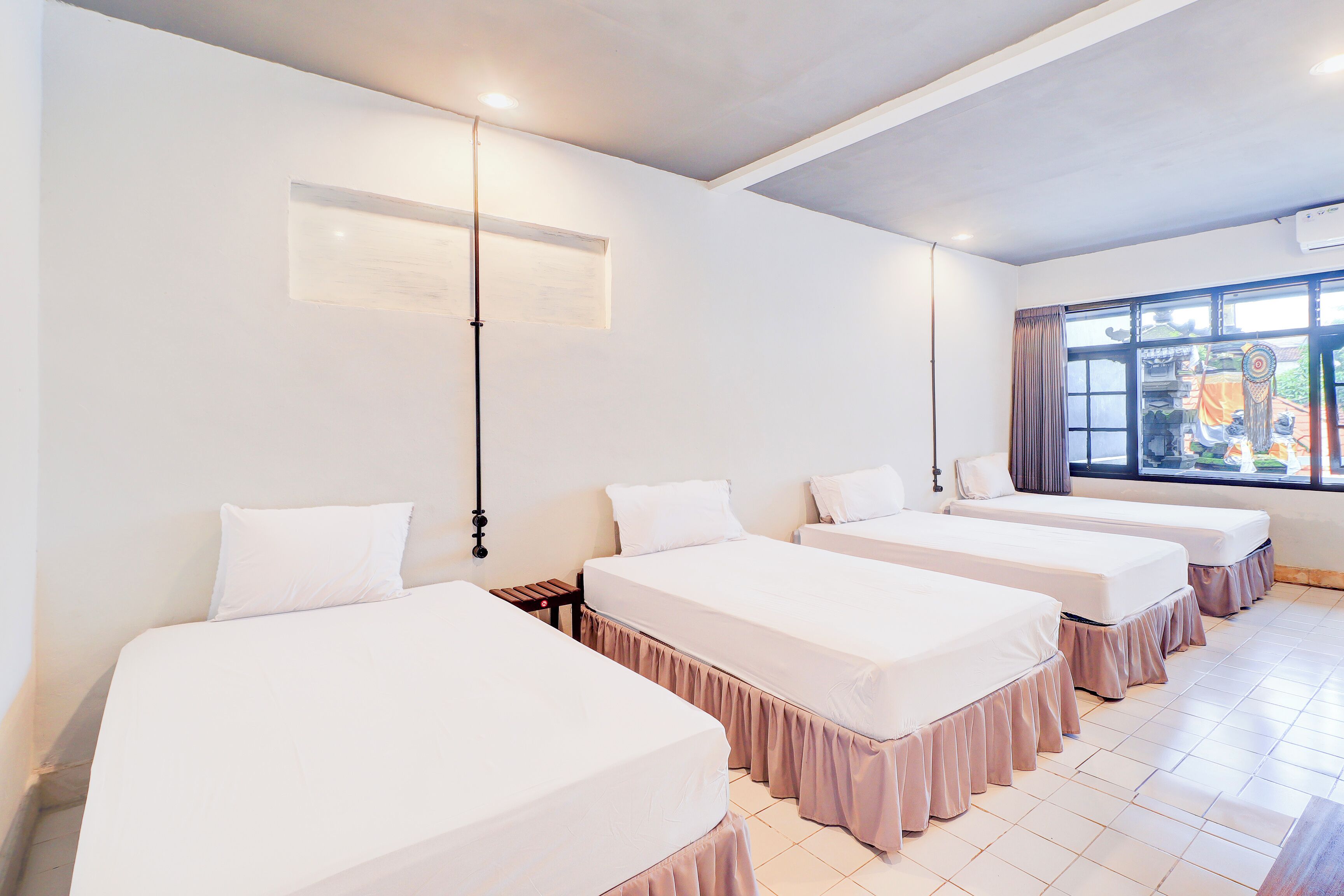 A hotel room with four beds arranged in a row, a small table, and a window with curtains.