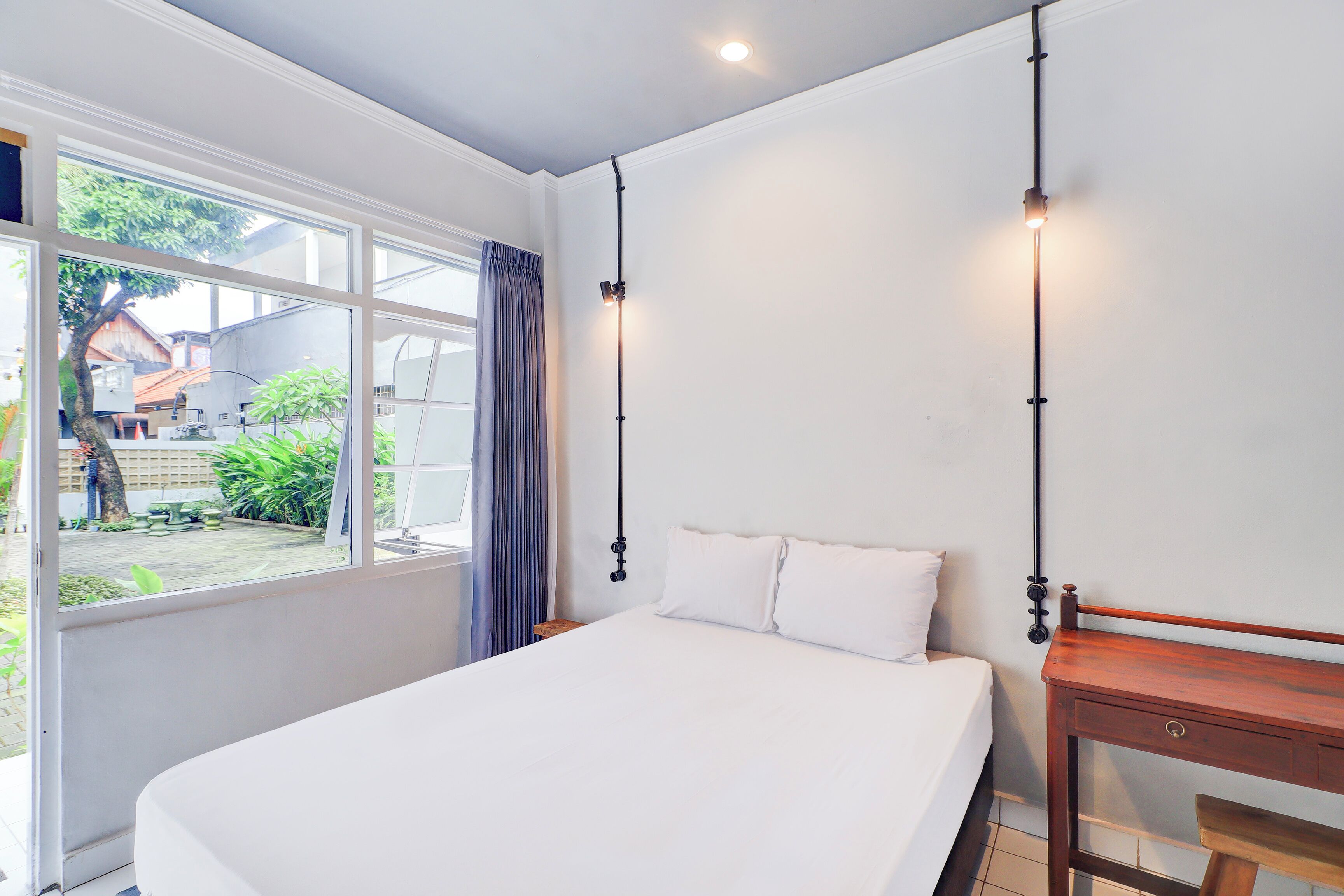 A bedroom with a large bed, a wooden nightstand, a desk, and a window with a view of the outside.