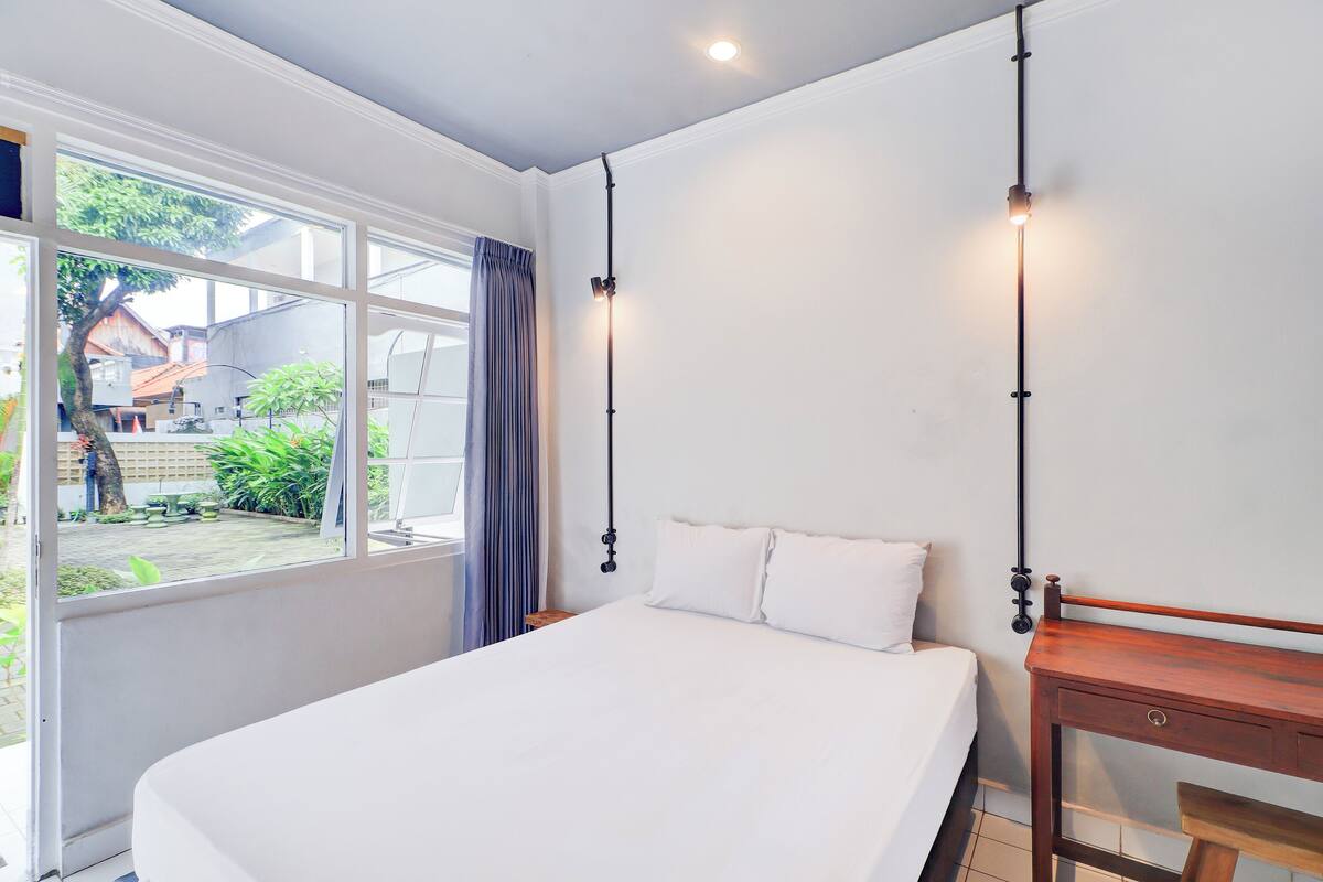 Ein Schlafzimmer mit einem großen Bett, einem hölzernen Nachttisch, einem Schreibtisch und einem Fenster mit Blick nach außen.