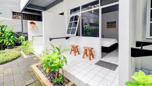 Una habitación moderna y compacta con una cama, dos taburetes de madera y una ventana.