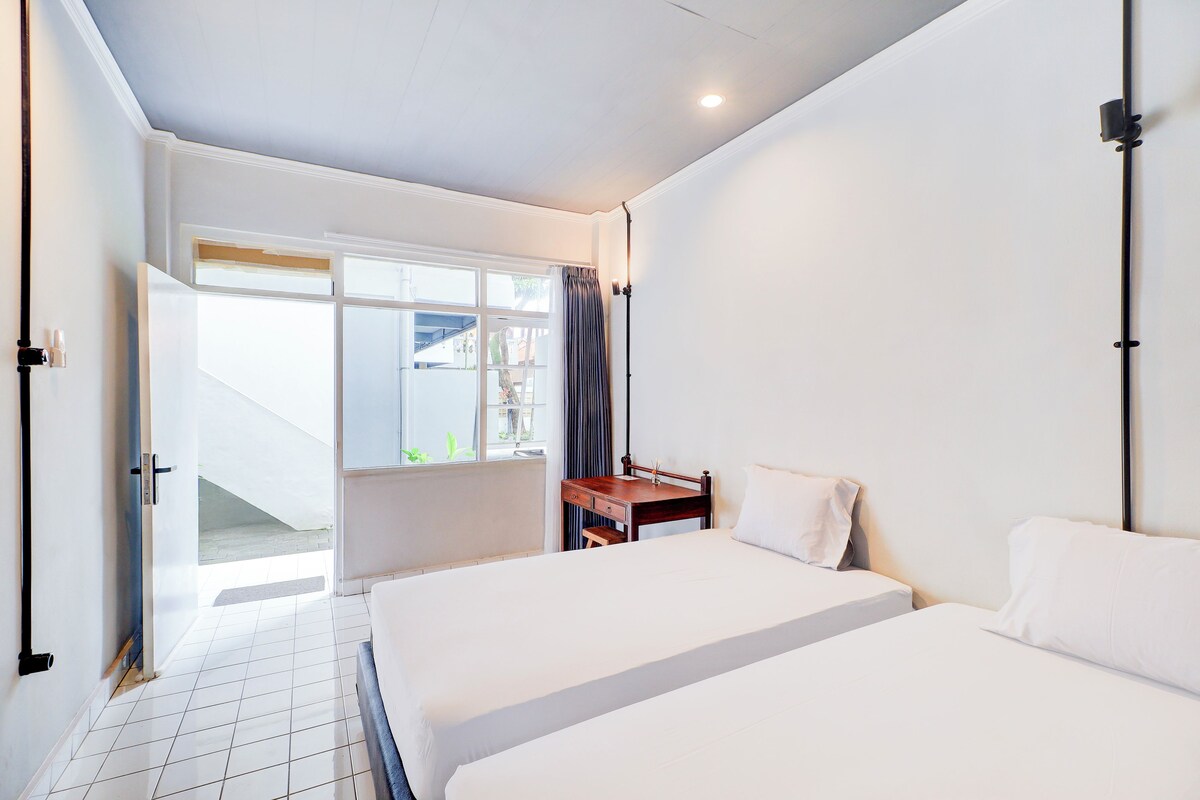 Habitació d'hotel amb dos llits, una taula de treball i una finestra amb cortines.
