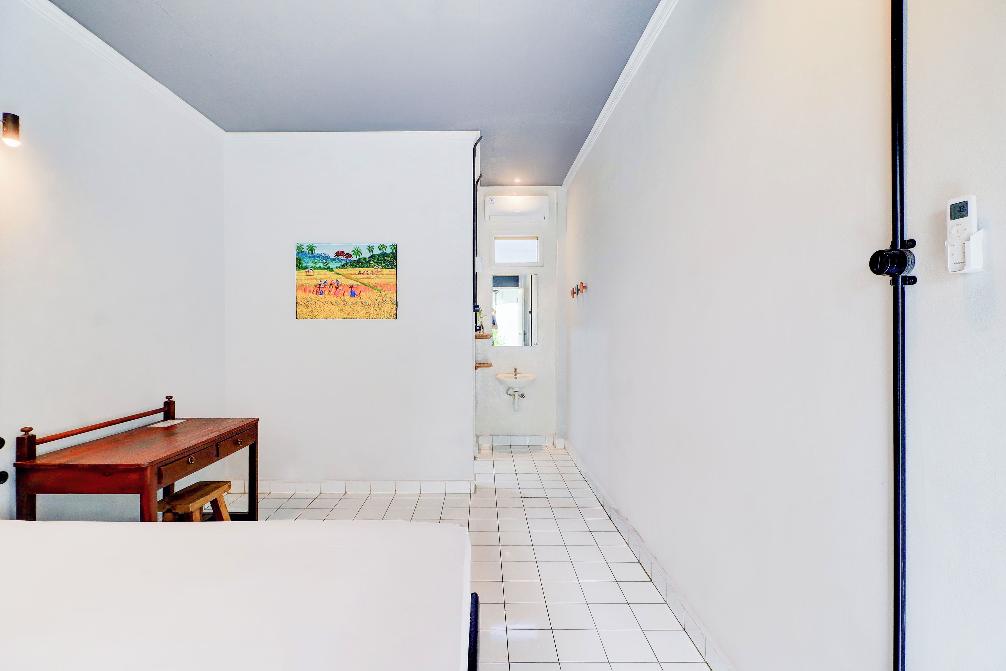 Un couloir avec un banc en bois, un tableau accroché au mur et une salle de bain visible au loin.