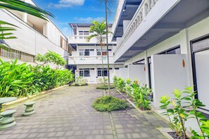 A courtyard with a paved walkway, potted plants, and a building with multiple balconies and windows. - Collection O At Jalan Padma Legian Beach (Legian)
