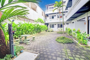 A courtyard with a paved walkway, potted plants, and a stone table.