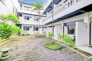A courtyard with a paved walkway, potted plants, and a stone bench.