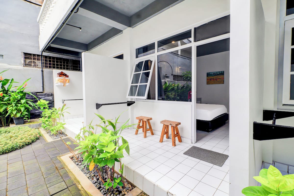 A modern, compact room with a bed, two wooden stools, and a window.