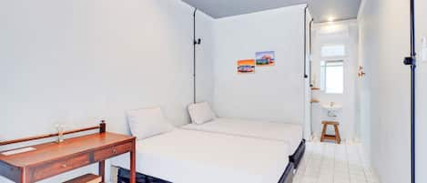 A bedroom with a bed, a desk, and a small stool. There is a window with a view of a building and a painting on the wall.
