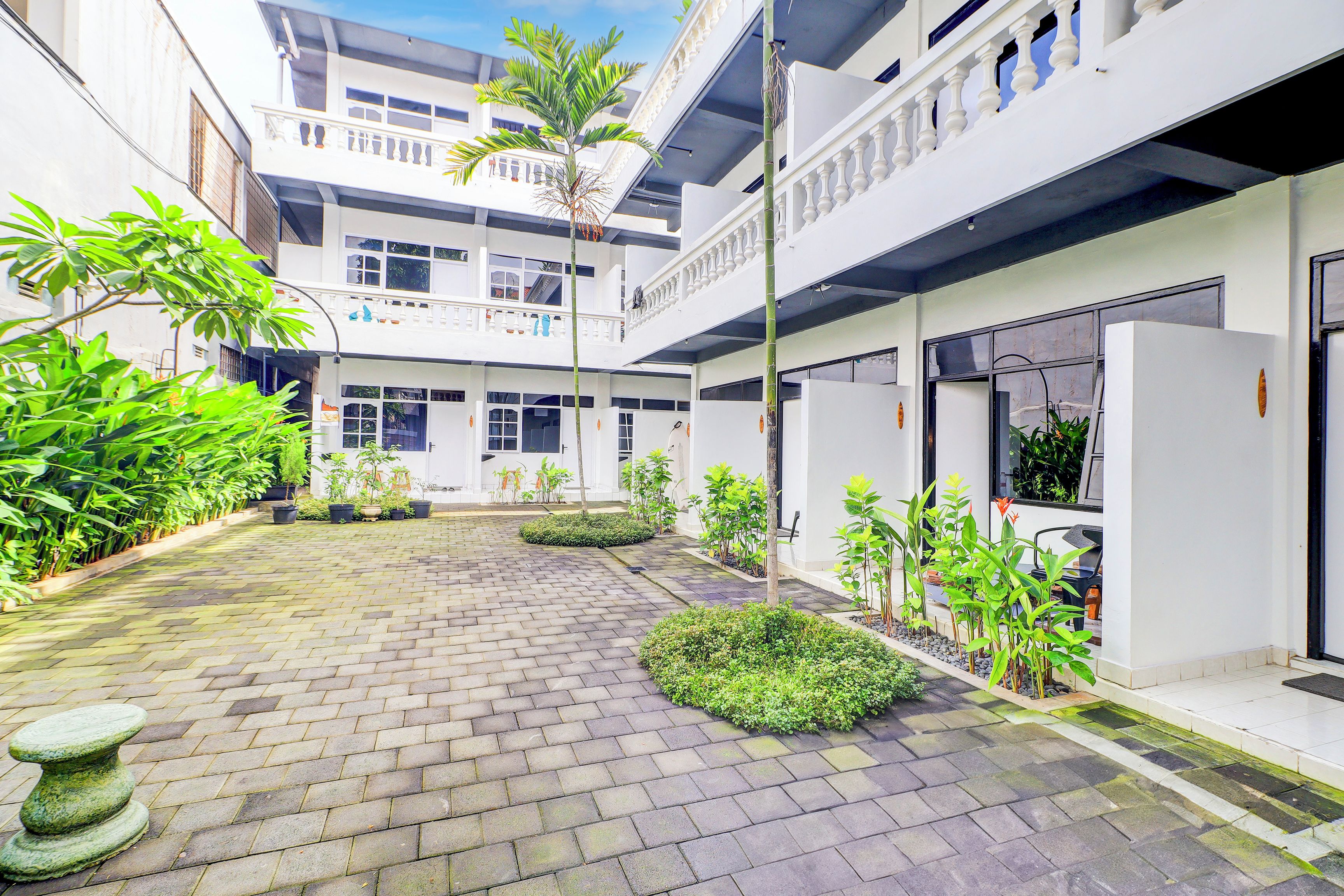 A courtyard with a paved walkway, potted plants, and a stone bench.