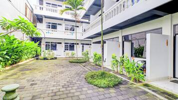 A courtyard with a paved walkway, potted plants, and a stone bench.