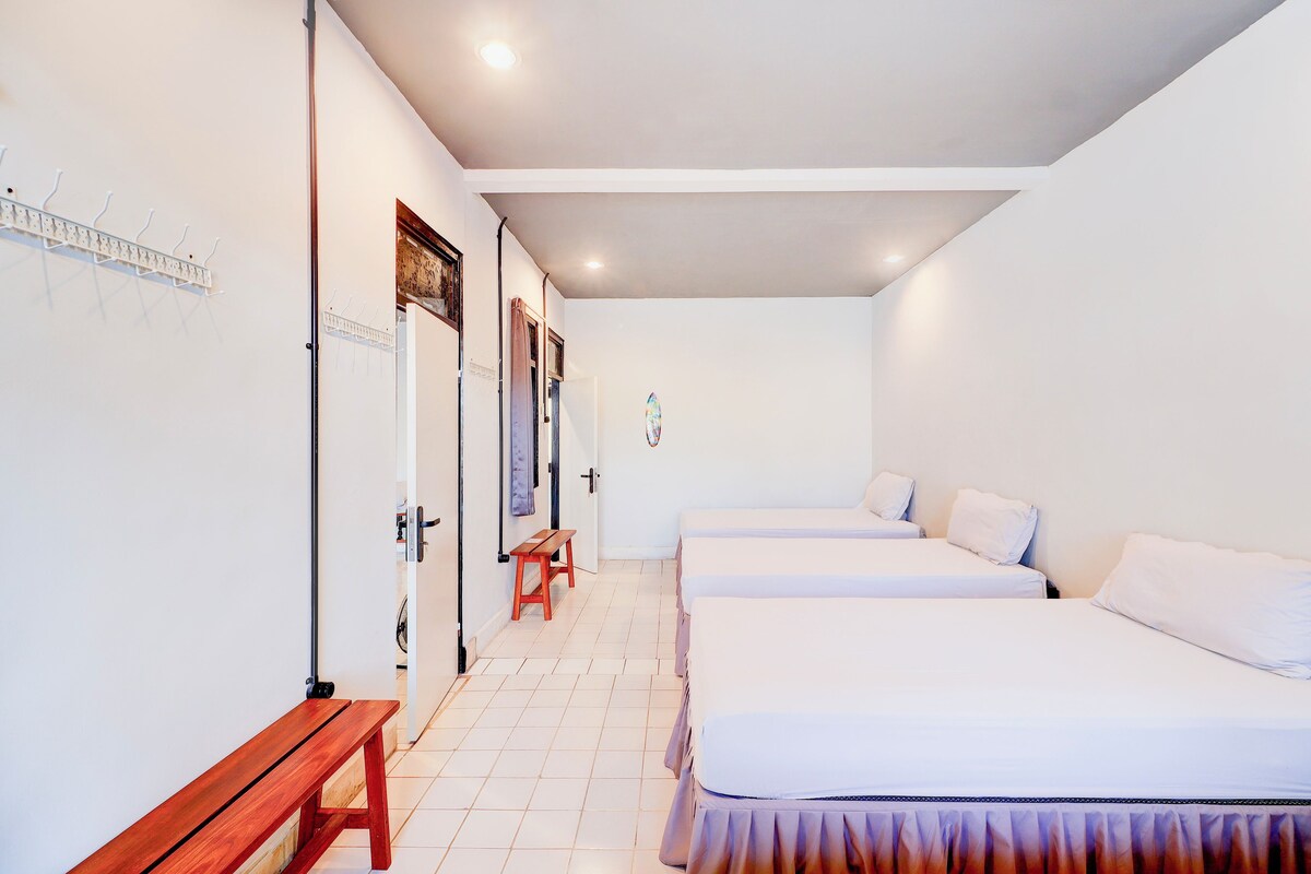Habitació d'hotel amb tres llits, una panxa de fusta i un banc a prop de la porta.