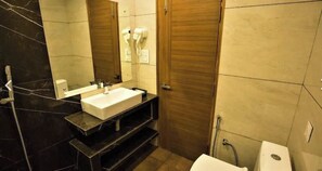 A bathroom with a white sink, a mirror, a towel rack, and a shower area. - Hotel Coral Star (Chandigarh)