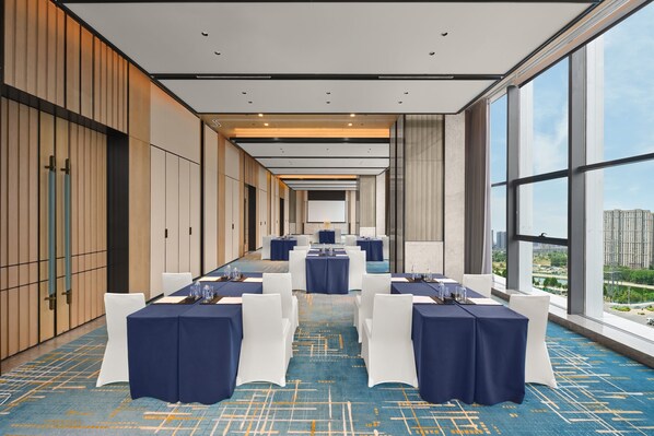 Uma sala de conferências com mesas dispostas para uma reunião, grandes janelas com vista para a cidade e design de interiores moderno.