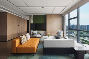 Una sala de estar moderna con un sofá, sillas, una mesa de centro y vistas de un paisaje urbano a través de amplios ventanales.