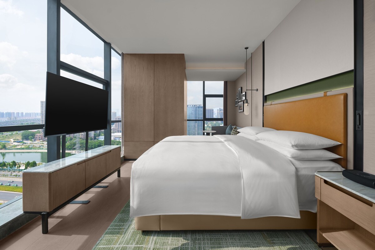 Une chambre d’hôtel moderne dotée d’un grand lit, d’une télévision à écran plat et offrant une vue sur la ville.