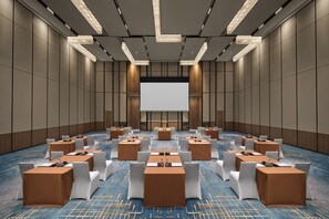 A conference room with a large screen, multiple tables with chairs, and a carpeted floor. - Doubletree by Hilton Zhengzhou East (Zhengzhou)