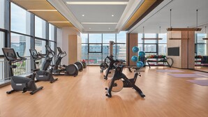 Un gimnasio con equipamiento de ejercicio, ventanas amplias y vista a la ciudad.