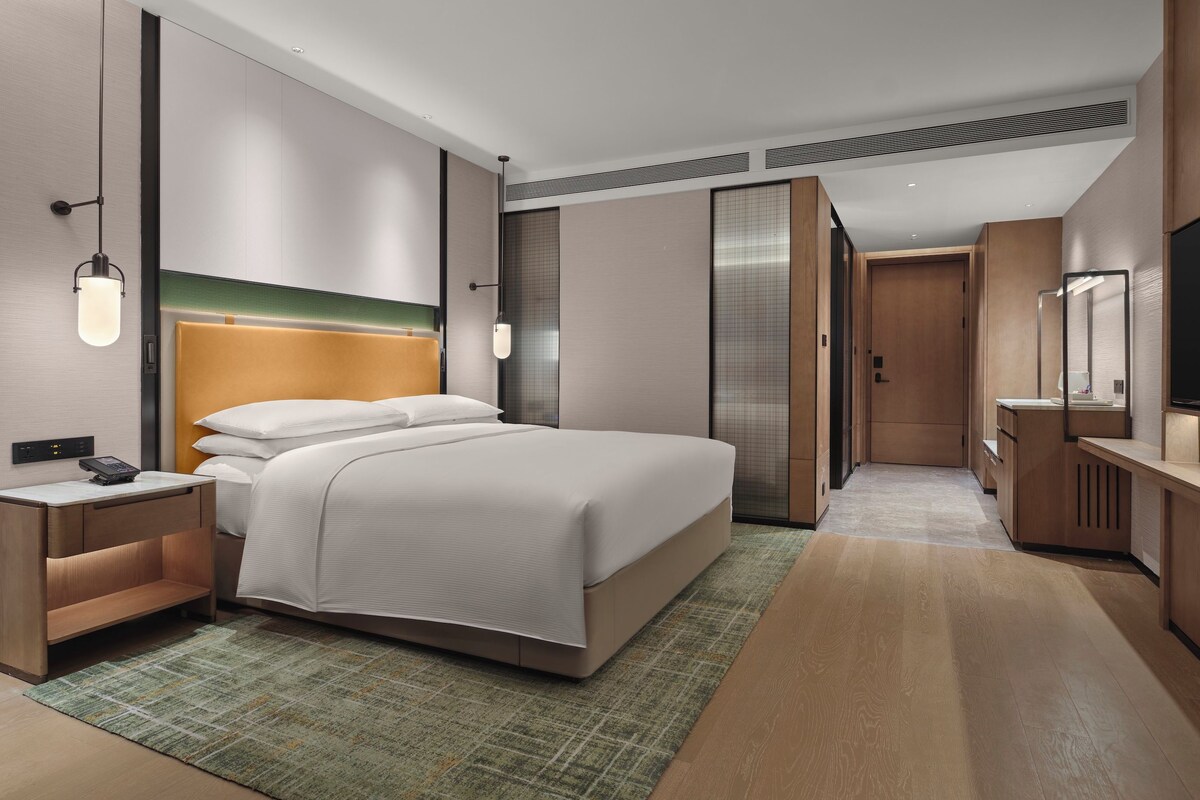 A modern hotel room with a large bed, bedside tables, a flat-screen TV, and a walk-in closet.