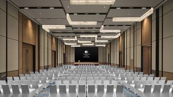 A conference room with rows of white chairs, a stage with a screen, and modern lighting fixtures.