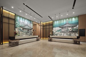 Zona de recepción con un gran mural de arquitectura tradicional, un mostrador de mármol y un diseño de iluminación moderno.