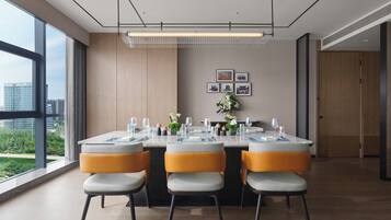 A modern dining area with a large table set for four, surrounded by chairs with cushioned seats and metal legs.