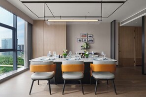 A modern dining area with a large table set for four, surrounded by chairs with cushioned seats and metal legs. - Doubletree by Hilton Zhengzhou East (Zhengzhou)