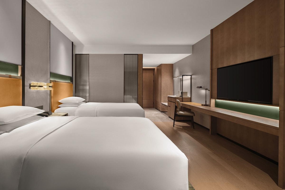 Habitación de hotel con dos camas, un escritorio, una silla, un televisor y un armario.