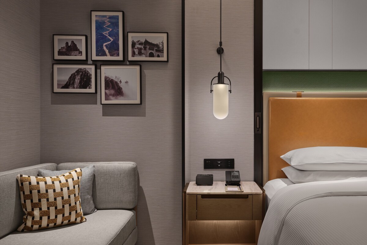 A modern bedroom with a bed, a nightstand with a lamp, and a wall with framed pictures.