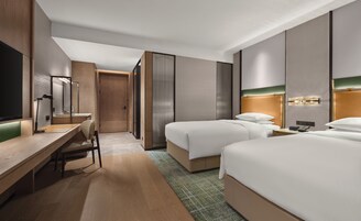 Una habitación de hotel con escritorio, dos camas, espejo y televisor.