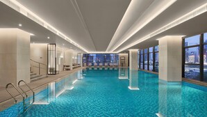 Una piscina interior con agua azul cristalina, ventanas amplias y vistas a la ciudad.