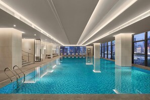 An indoor swimming pool with clear blue water, large windows, and a city view. - Doubletree by Hilton Zhengzhou East (Zhengzhou)