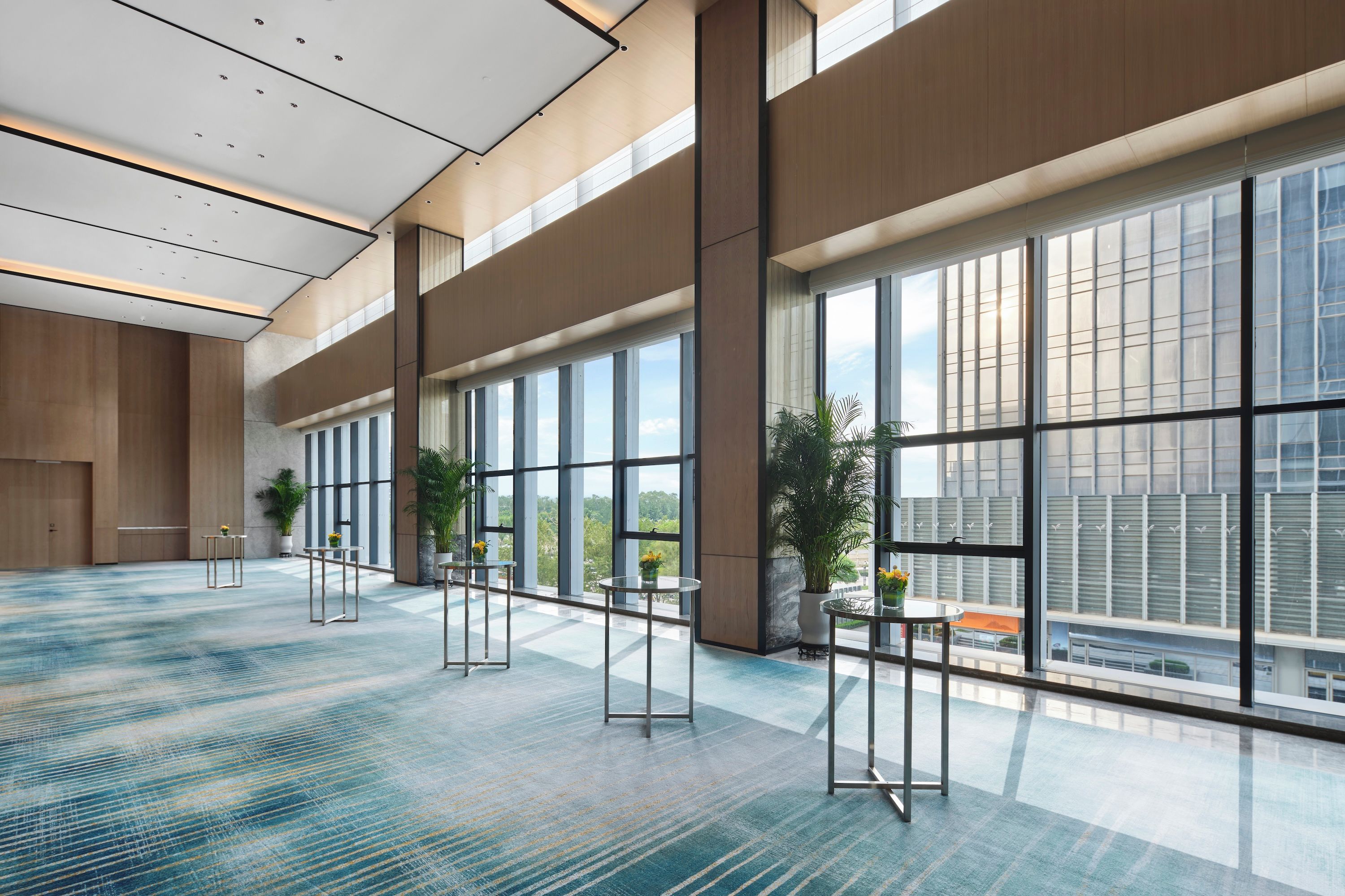 A spacious indoor area with large windows, a patterned carpet, and several tables with chairs.