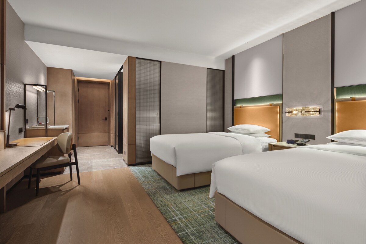 A hotel room with a desk, two beds, a mirror, and a TV.