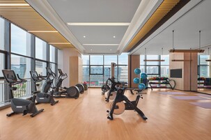 Un gimnasio con equipamiento de ejercicio, ventanas amplias y vista a la ciudad.