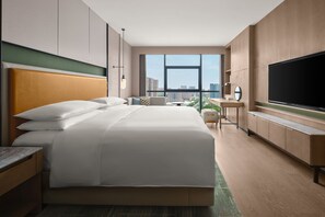 Een hotelkamer met een groot bed, een televisie, een bureau en uitzicht op de stad.