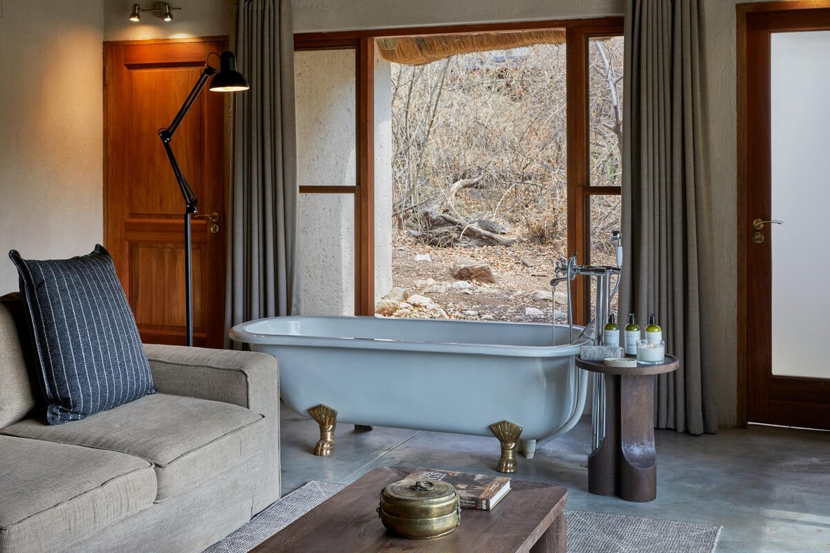 A room with a bathtub, a sofa, a lamp, and a view of the outdoors.