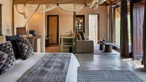 A spacious bedroom with a large bed, a sitting area with a table and chairs, and a view of the outdoors. - Toro River Lodge (Kareeberg)