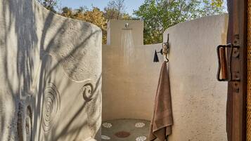 A stone-walled bathroom with a shower, a towel rack, and a circular mosaic floor.