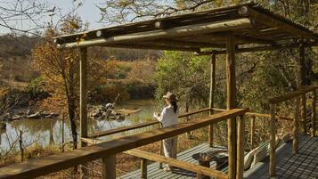 A wooden deck with a pergola, overlooking a body of water and a forested area.